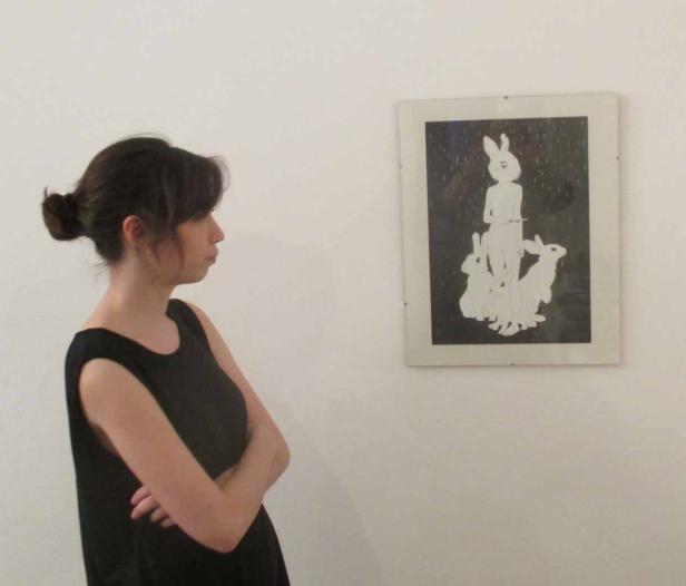 Eine Frau betrachtet ein gerahmtes Bild mit einer Figur und mehreren Hasen.