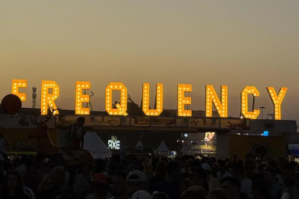 Menschenmenge vor leuchtendem "FREQUENCY"-Schriftzug beim Festival in der Abenddämmerung.