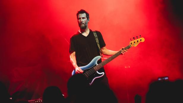 Ein Mann steht mit E-Gitarre auf einer Bühne mit rotem Hintergrund.