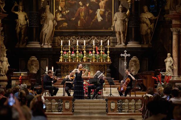 Streichquartett spielt vor Publikum im barocken Innenraum einer Kirche mit Altar und Kerzen.