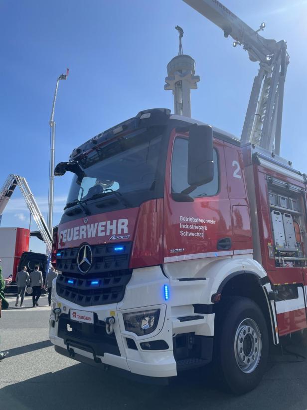 Ein modernes Feuerwehrfahrzeug der Betriebsfeuerwehr Industriepark Schwechat steht auf dem Außengelände der Interschutz-Messe in Hannover, umgeben von Hubrettungsfahrzeugen.