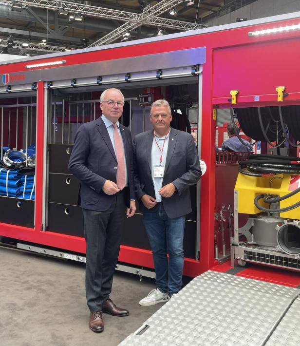 Zwei Männer stehen vor einer modernen Feuerwehr-Großpumpe auf einer Messehalle.