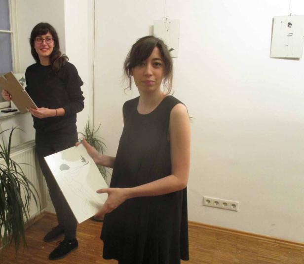Zwei Frauen präsentieren Zeichnungen in einer Galerie.