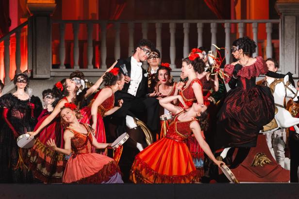 Mehrere Personen in rotem Gewand tanzen auf einer Bühne Flamenco.