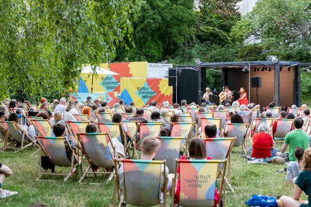 Publikum sitzt auf Liegestühlen vor einer Open-Air-Bühne beim Kultursommer Wien im Park.