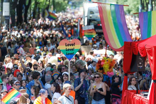 Große Menschenmenge bei der Regenbogenparade mit bunten Fahnen und Schildern in Wien.