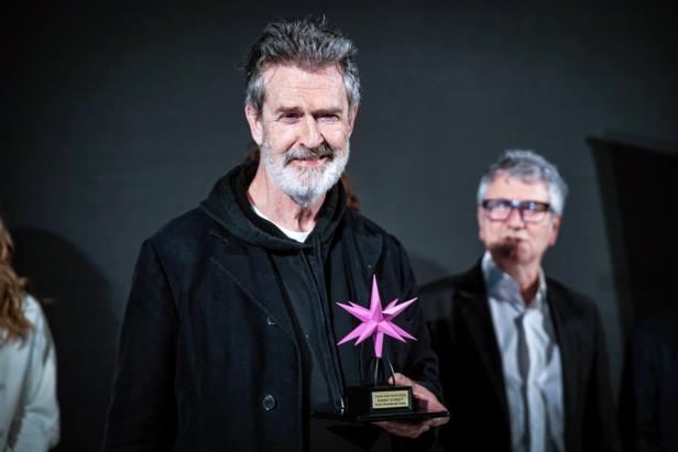 Rupert Everett mit grauen Haaren trägt eine schwarze Jacke.
