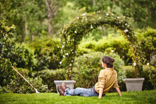 Frau sitzt im Gras und bewundert ihren Garten