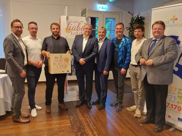 Acht Männer stehen nebeneinander in einem Raum, einer hält ein Schild mit der Aufschrift „Mein Südburgenland“.