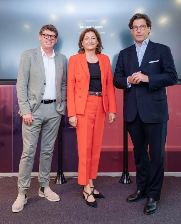 Drei Personen in Businesskleidung stehen nebeneinander vor einem Bildschirm mit der Aufschrift „Manager Forum“.