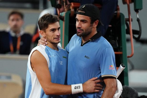 Zwei Tennisspieler in blauen Trikots umarmen sich nach einem Match auf dem Platz.