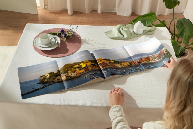 Eine Person betrachtet ein Fotobuch mit einer Panoramaaufnahme einer bunten Küstenstadt.