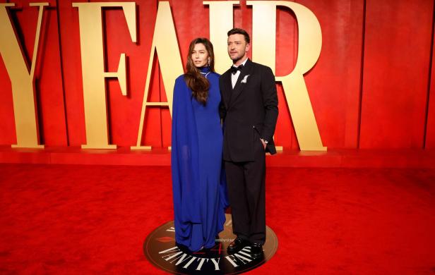 Jessica Biel in einem blauen Kleid und Justin Timberlake im schwarzen Anzug posieren vor dem Vanity Fair-Schriftzug auf einem roten Teppich.