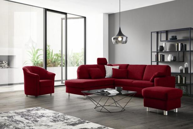 Modulares rotes Sofa mit passendem Sessel und Hocker in modernem Wohnzimmer, das flexible Einrichtungsmöglichkeiten bei XXXLutz zeigt.