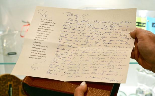 Zwei Hände halten einen handgeschriebenen Brief mit einem gedruckten Gedicht und einem gezeichneten Herz in einer hellen Umgebung.
