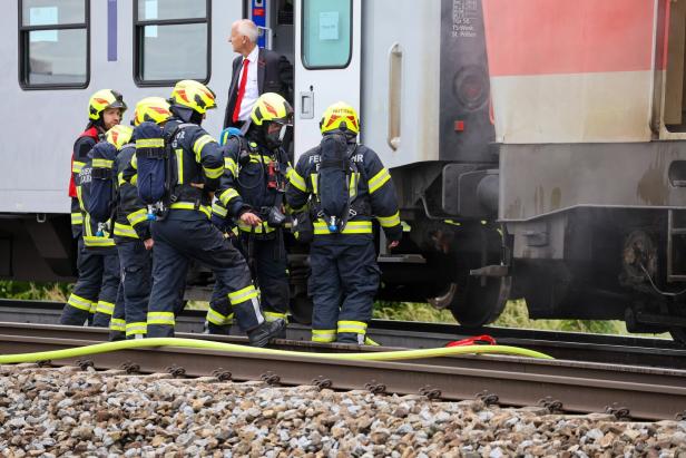 Mehrere Feuerwehrleute in Schutzkleidung stehen an einem Zug auf den Gleisen, während ein Mann im Anzug an der Tür steht.