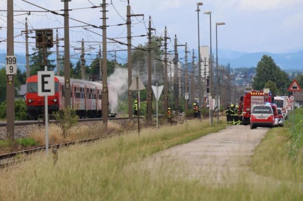 Ein roter Zug steht auf den Gleisen, Feuerwehrleute und Einsatzfahrzeuge sind wegen Rauchentwicklung im Einsatz.