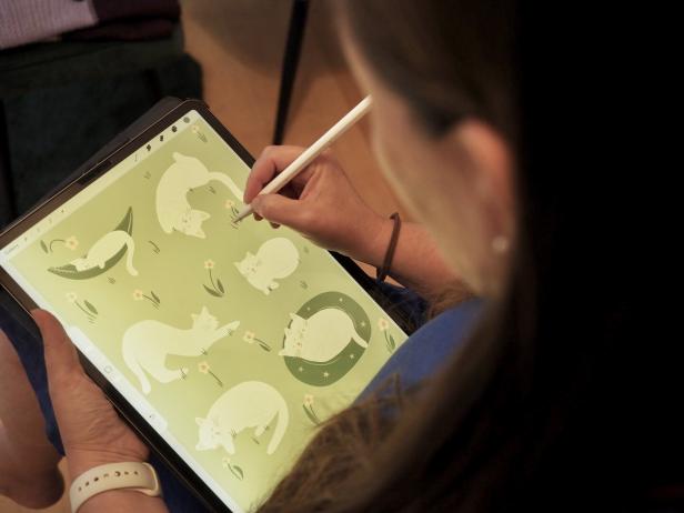 Eine Person zeichnet mit einem Stift auf einem Tablet mehrere weiße Katzen in verschiedenen Posen auf grünem Hintergrund.