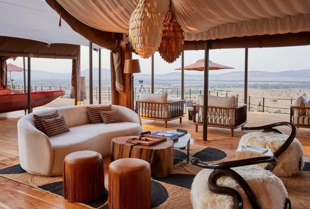 Gemütliche Lounge mit modernen Möbeln, Holztischen und Blick auf eine weite Savannenlandschaft durch große Fenster.