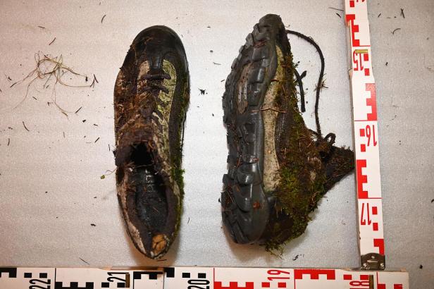 Zwei stark verschmutzte, abgenutzte Sportschuhe mit Moos und Erde neben Maßband.