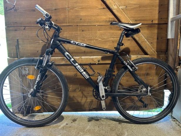 Schwarzes Cube-Fahrrad mit weißer Aufschrift steht vor einer Holzwand.