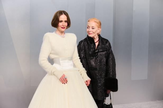 Sarah Paulson in einem cremefarbenen Kleid und Holland Taylor in einer schwarzen Jacke stehen nebeneinander vor einem grauen Hintergrund.