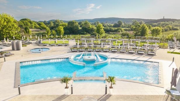 Großer Außenpool mit Liegen und Sonnenschirmen vor grüner Landschaft im Spa-Bereich.