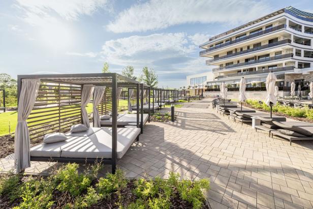 Moderne Liegebereiche und Sonnenliegen vor einem luxuriösen Hotel bei sonnigem Wetter.