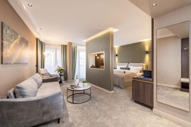 Modernes, stilvoll eingerichtetes Hotelzimmer mit Wohnbereich, Doppelbett und großen Fenstern.