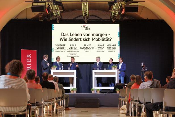 Fünf Männer diskutieren auf einer Bühne vor Publikum über die Zukunft der Mobilität, hinter ihnen eine große Präsentationsfolie.