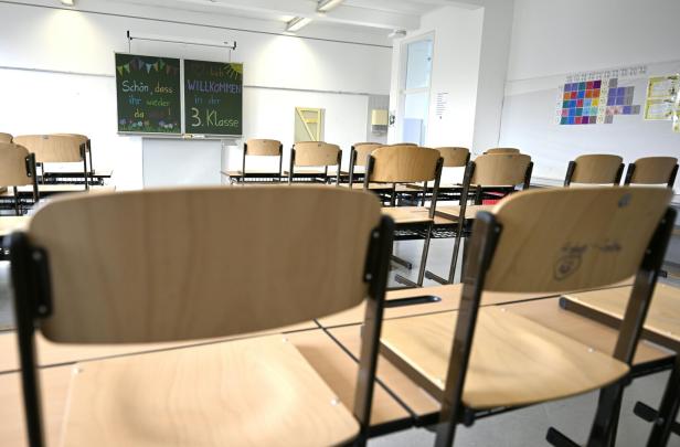 Leerer Klassenraum mit hochgestellten Stühlen und einer Tafel, auf der eine Willkommensbotschaft für die 3. Klasse steht.