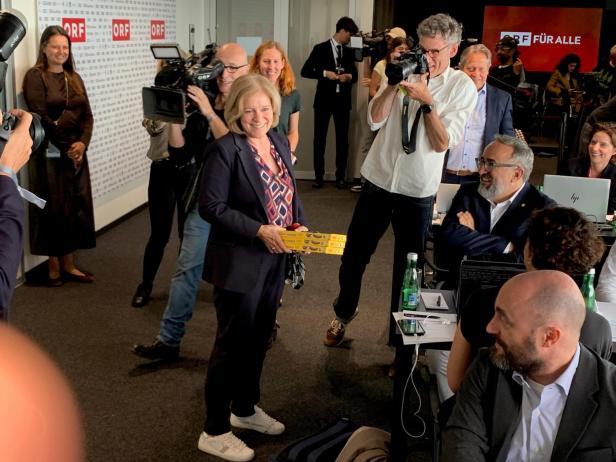 Ingrid Thurnher im dunklen Anzug bringt wartenden Journalisten Schokobananan
