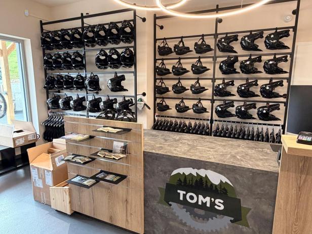 Verkaufsraum mit Wandregalen voller Fahrradhelme und einem Verkaufstresen mit Logo 'TOM'S'.