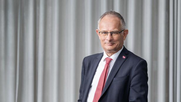 Markus Marterbauer steht vor einem hellen Vorhang und lächelt leicht.