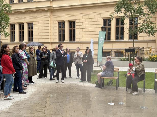 Eine Gruppe von Menschen versammelt sich vor einem historischen Gebäude in Wien Neubau, während ein Mann mit Mikrofon eine Ansprache hält.