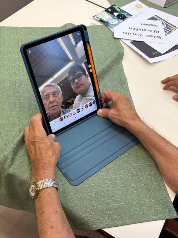 Senior und Jugendlicher betrachten gemeinsam ein Selfie mit Filtern auf einem Tablet, bevor ihre Gesichter vertauscht werden