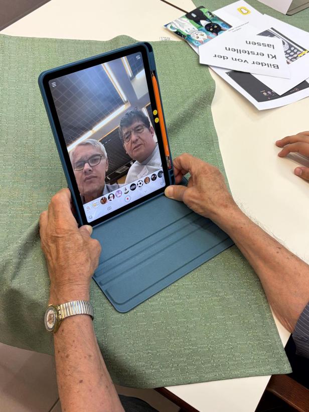 Senior und Jugendlicher betrachten gemeinsam ein Selfie mit Filtern auf einem Tablet. nchdem ihre Gesichter vertauscht wurden.