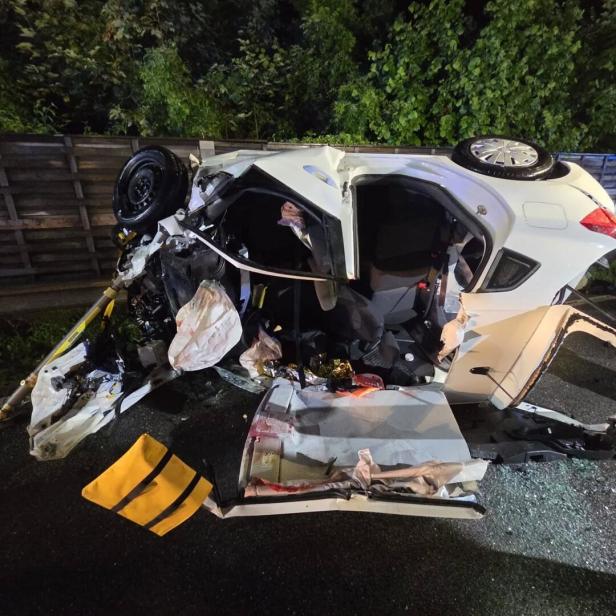 Ein stark beschädigtes weißes Auto liegt auf der Seite, umgeben von Trümmern und aufgerissenen Autoteilen.