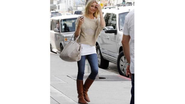Cameron Diaz mit braunen Stiefeln, Jeans und beigem Pullover auf dem Bürgersteig.