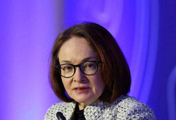 Frau mit braunen Haaren und Brille spricht vor einem Mikrofon vor blau-violettem Hintergrund.