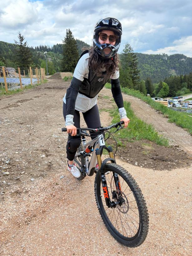 Person mit Helm, Schutzweste und Knieschützern auf Mountainbike auf einem Schotterweg in bergiger Landschaft