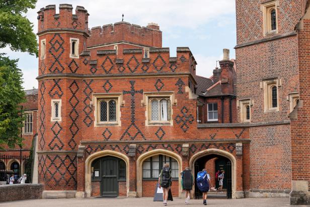 Schüler mit großen Rucksäcken gehen auf ein historisches Backsteingebäude mit Zinnen und Rautenmuster - das Eton College - zu.