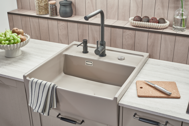 Helle Küchenspüle mit hohem Wasserhahn, Handtuch an der Spüle, Obstschale und Schneidebrett auf der Arbeitsplatte.