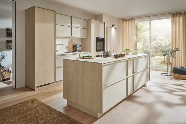 Helle Wohnküche mit heller Holzoptik, großer Kochinsel und bodentiefem Fenster, passend zur mömax-Küchenplanung.
