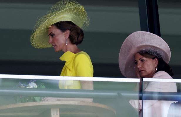 Kate, Prinzessin von Wales, in einem gelben Kleid mit Hut neben Carole Middleton in einem hellrosa Outfit auf einer Tribüne.