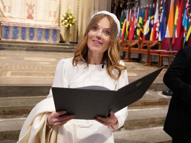 Geri Halliwell-Horner trägt beim Commonwealth Day Service of Celebration ein weißes Kleid mit passendem Fascinator und hält ein aufgeschlagenes Buch in einer Kirche vor zahlreichen Flaggen.