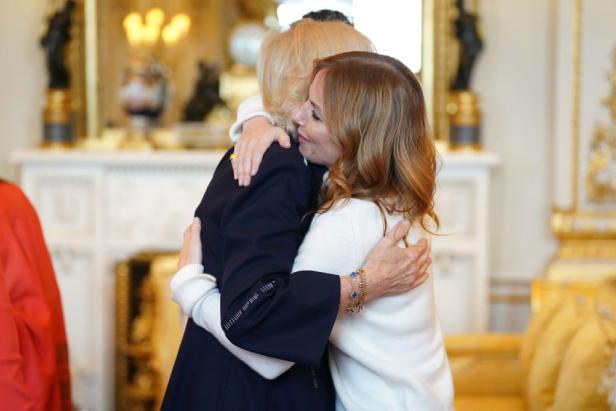 Königin Camilla umarmt herzlich Geri Halliwell in einem hellen Pullover in einem prunkvollen Raum.
