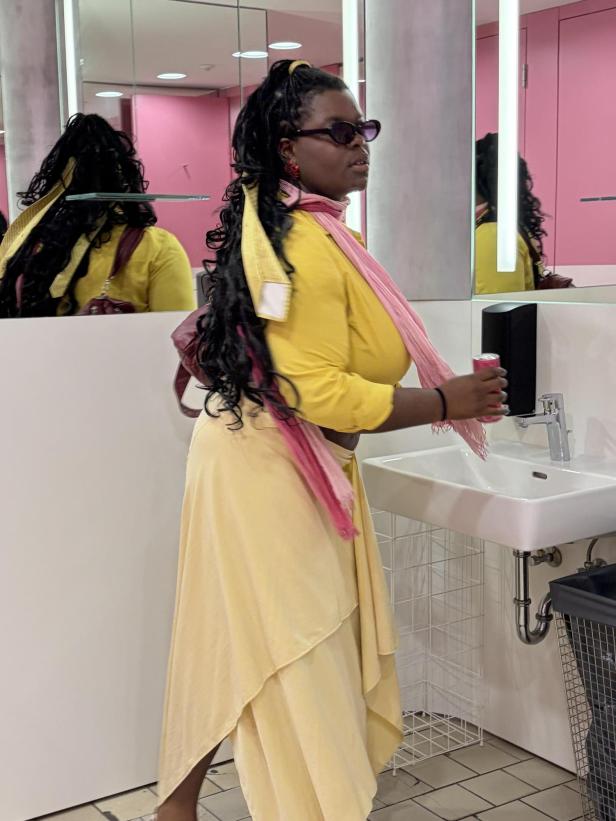 Frau in gelbem Kleid mit Sonnenbrille steht vor einem Spiegel