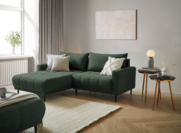 Ecksofa mit Chaiselongue und Kissen in modernem Wohnzimmer neben zwei kleinen Beistelltischen mit Dekoration