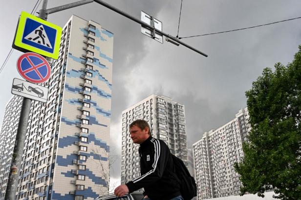 Mann geht vor Hochhäusern unter dunklem Himmel vorbei, links Verkehrszeichen und ein Abschleppschild.